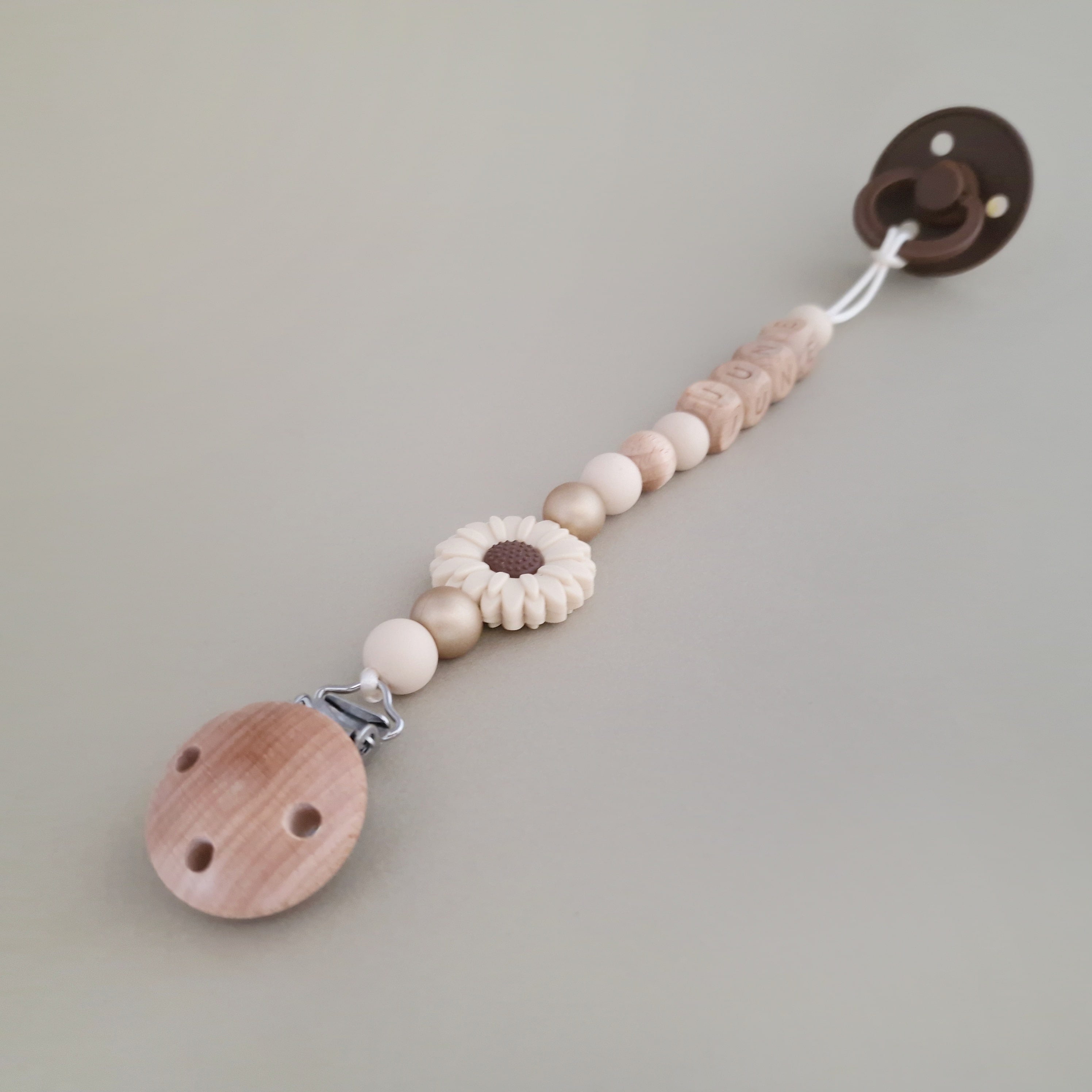 Speenkoord met naam van Studio Bambacht met bloem in de kleuren beige en goud