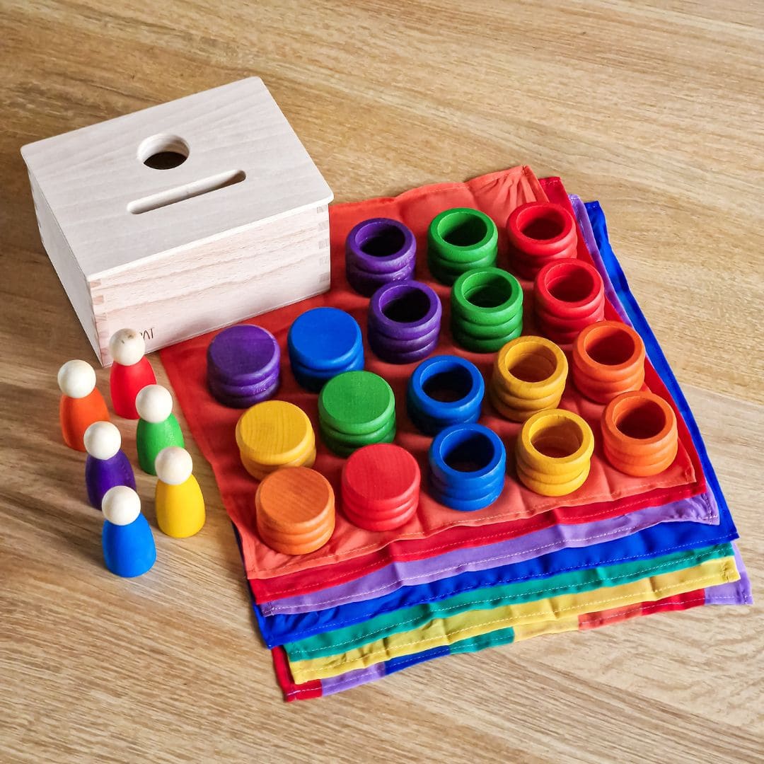 Open einde starterspeelset voor 0-2 jaar met objectpermanentiebox, speeldoek en grapat houten ringen, munten en poppetjes om objectpermantie te stimuleren en uit te nodigen tot fantasierijk en zelfstandig spel