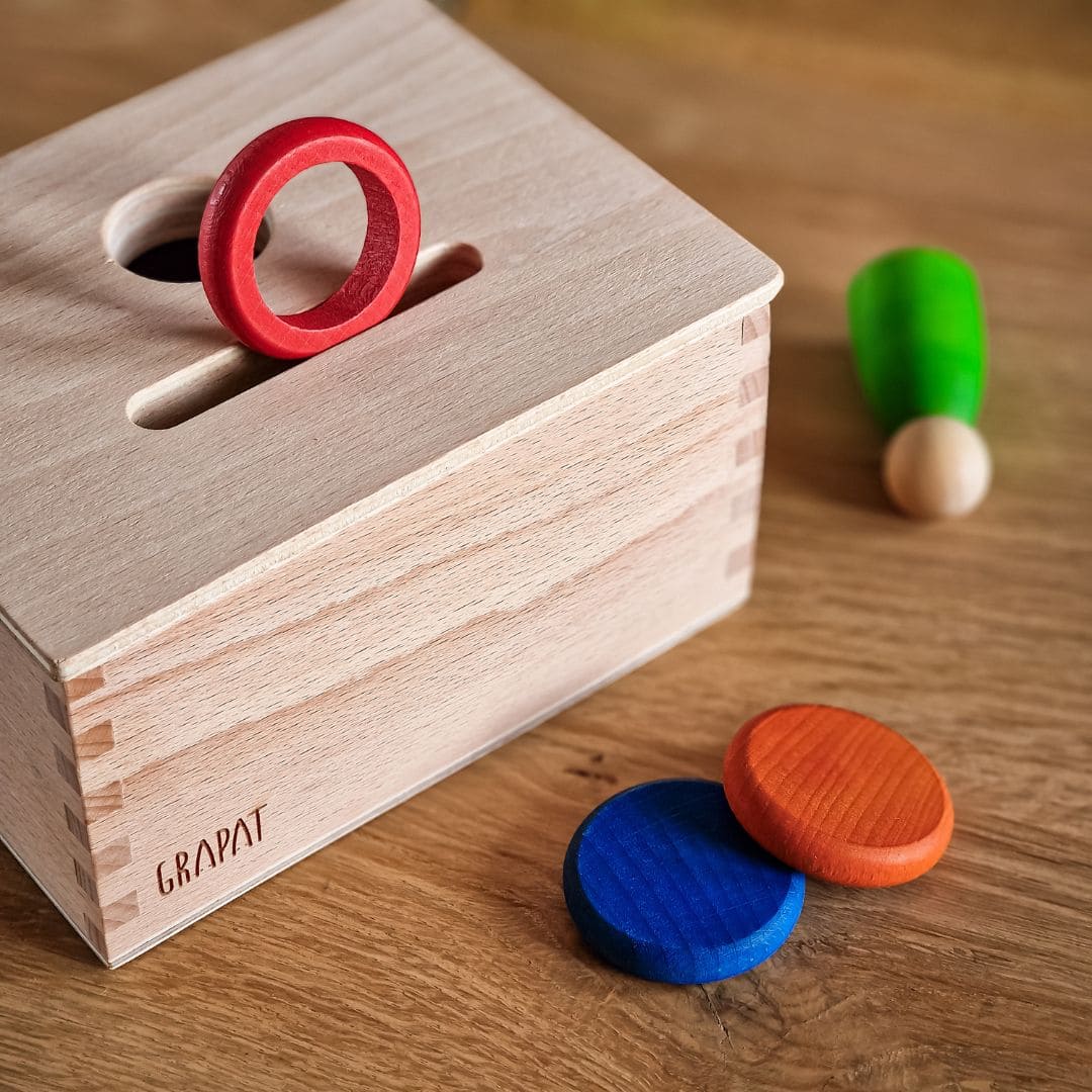 Open einde starterspeelset voor 0-2 jaar met objectpermanentiebox, speeldoek en grapat houten ringen, munten en poppetjes om objectpermantie te stimuleren en uit te nodigen tot fantasierijk en zelfstandig spel